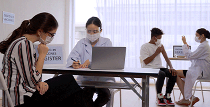 Four masked people working around laptops